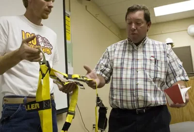 safety management student being shown how to use a body harness by safety management instructor