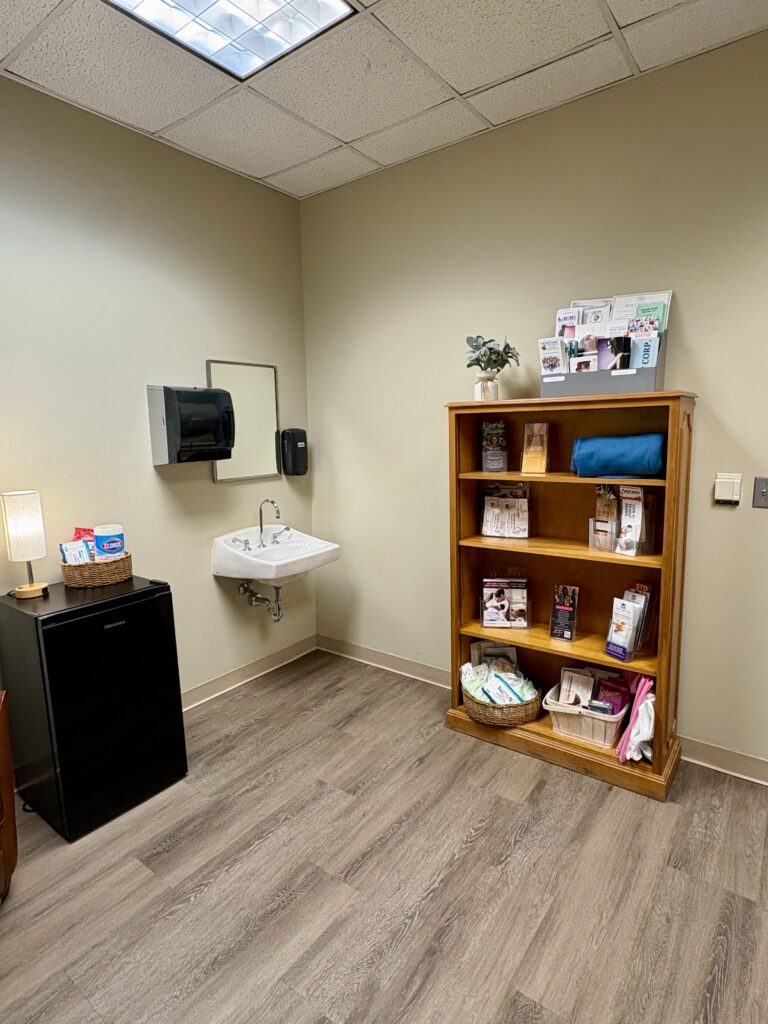 Lactation room with a mini refrigerator, bookshelf, sink, and wood-look flooring.