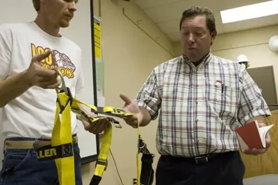 safety management student being shown how to use a body harness by safety management instructor
